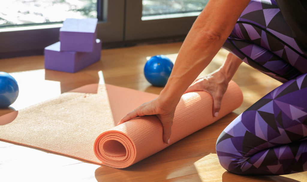 Woman Rolling A Yoga Mat On Wooden Floor